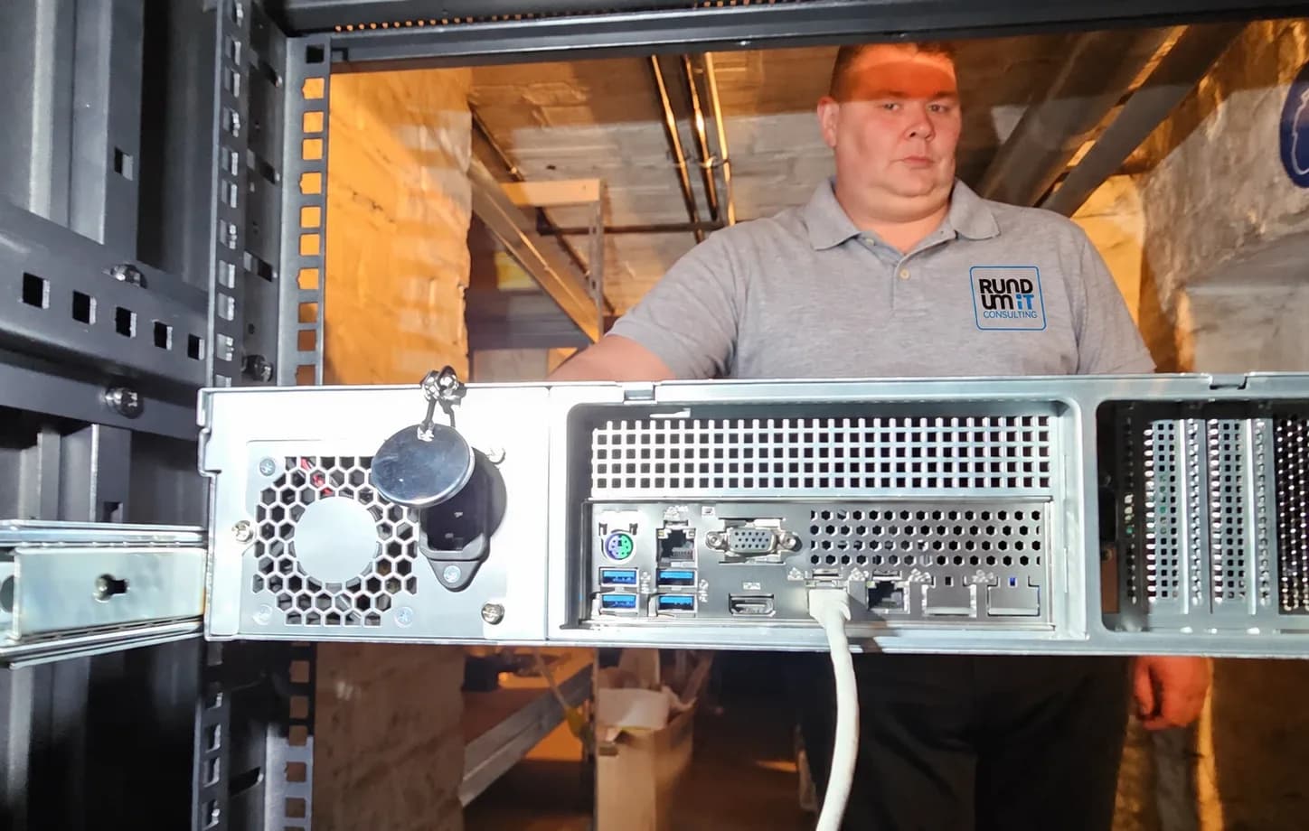 Swen Haas im Rundum-IT-Poloshirt hinter einem Server, der auf Schienen in einen Serverschrank eingebaut wird